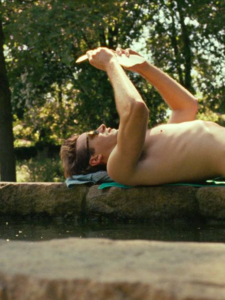 Oliver reads a book while lying on the edge of a small natural pool.