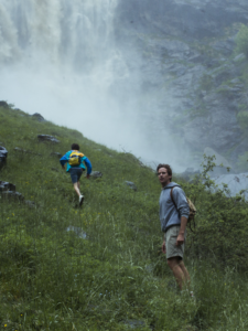 Elio and Oliver walking on grass with a waterfall in the background.