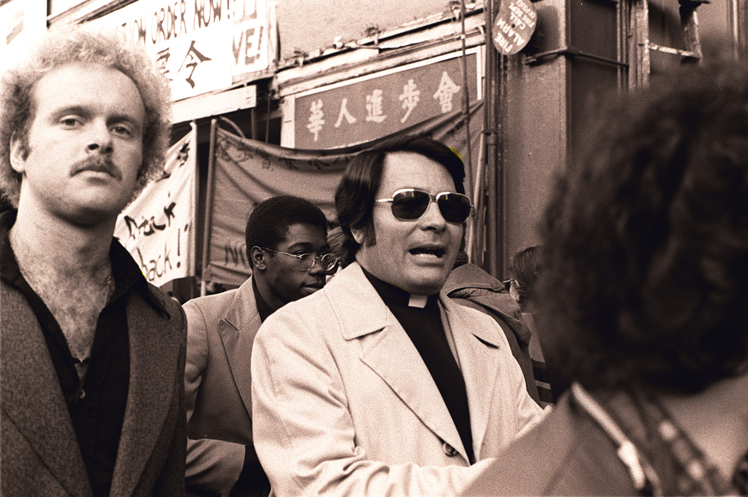 Il reverendo Jim Jones del Peoples Temple di San Francisco protesta contro lo sfratto forzato degli inquilini anziani dall'International Hotel, 848 Kearny Street vicino a Washington Street domenica 16 gennaio 1977. La guardia del corpo e figlio adottivo Tim Tupper è a sinistra. Viene mostrato anche Darrell Devers, un'altra guardia del Tempio. Foto di Nancy Wong